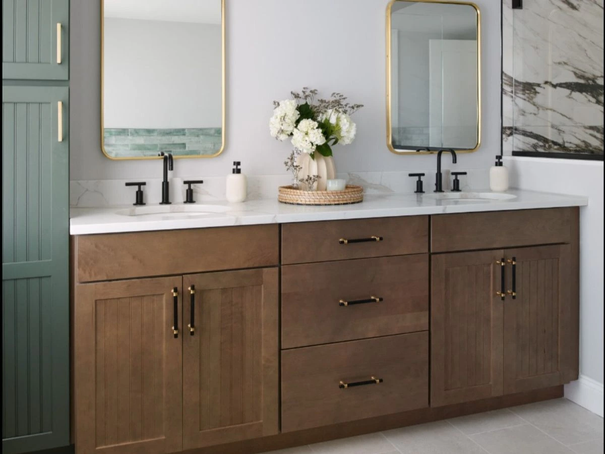 Elegant double-sink bathroom vanity with dark wood cabinetry, gold-accented mirrors, and black faucets, complemented by decorative greenery and neutral decor